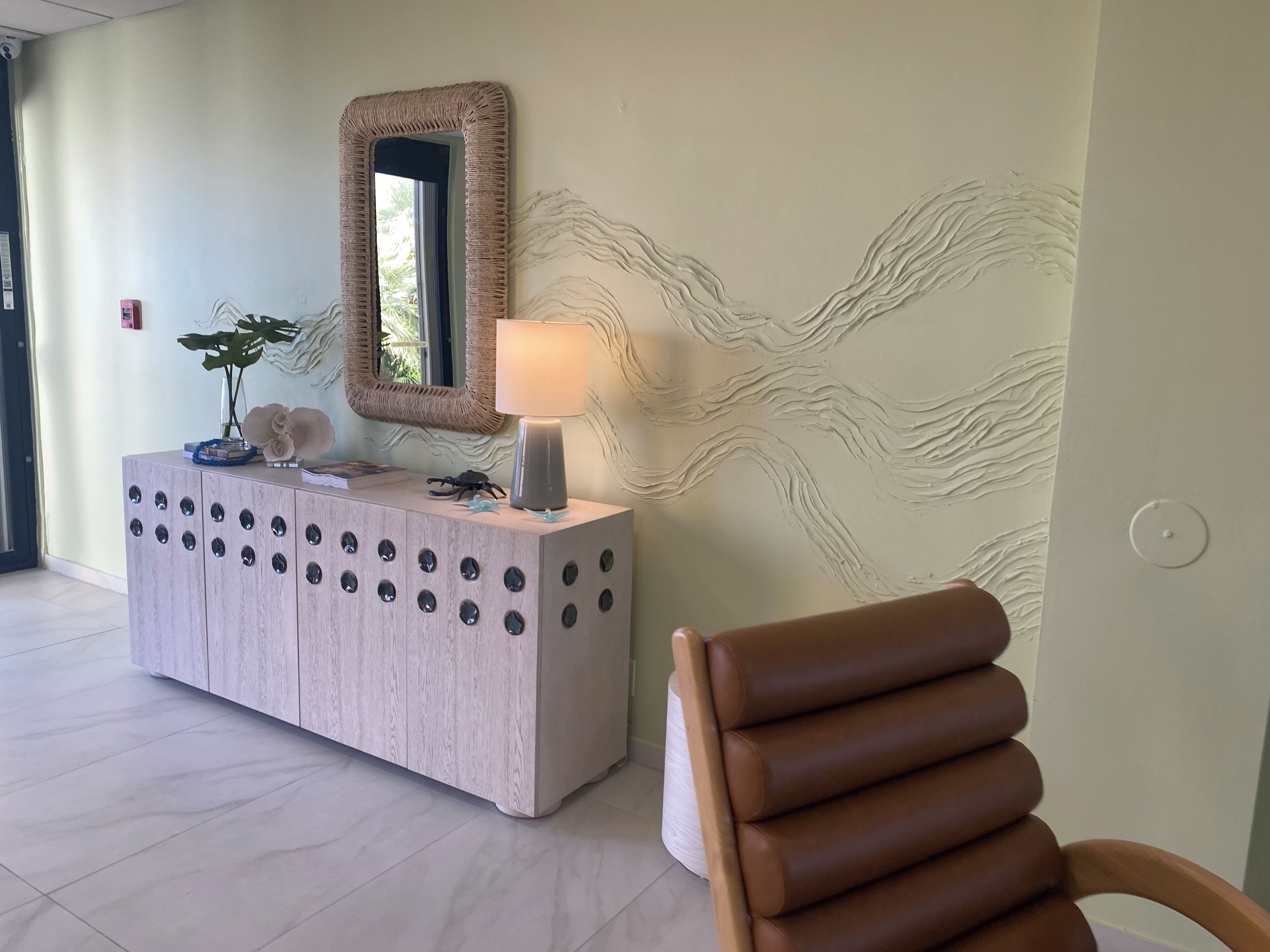 Una zona de recepción con una consola de madera, un espejo, una lámpara y una silla.