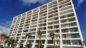 Un hotel de varios pisos con balcones, palmeras y un cielo azul despejado.