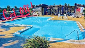 Una piscina con sillas de descanso y una zona sombreada con sombrillas.