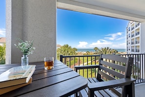 A balcony with a view of the ocean, a table with a book and a glass of drink, and a chair.