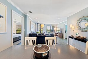 A modern living room with a dining table, a sofa set, and a kitchen area visible in the background.