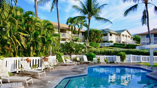 A pool area with lounge chairs, palm trees, and a building with balconies. - Mid-Term Stays in Gorgeous Condo
 Kona, Big Island (Kailua-Kona)