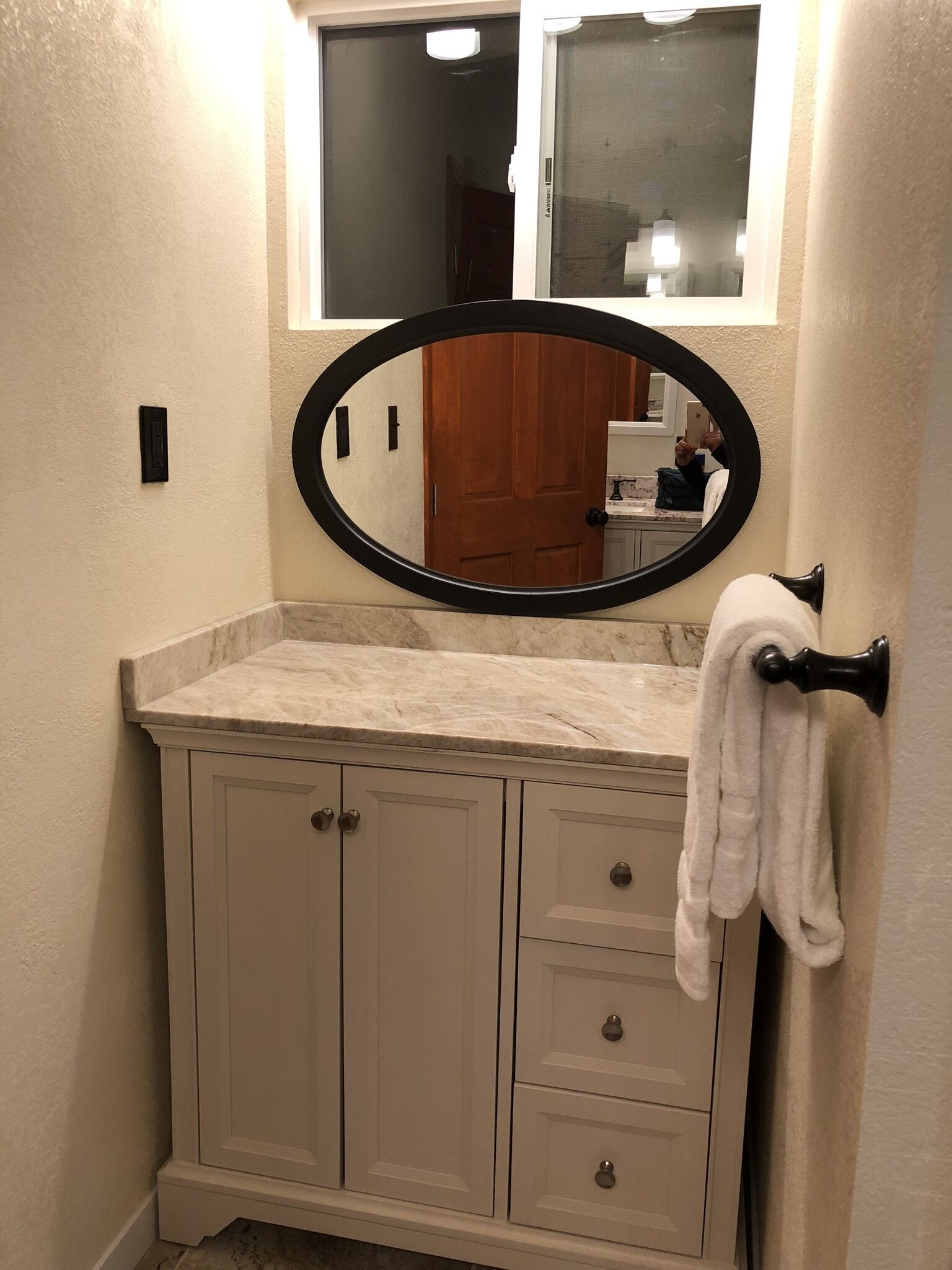 Une salle de bain avec un comptoir en marbre, un meuble-lavabo blanc doté de tiroirs, un miroir à cadre noir et un porte-serviettes.