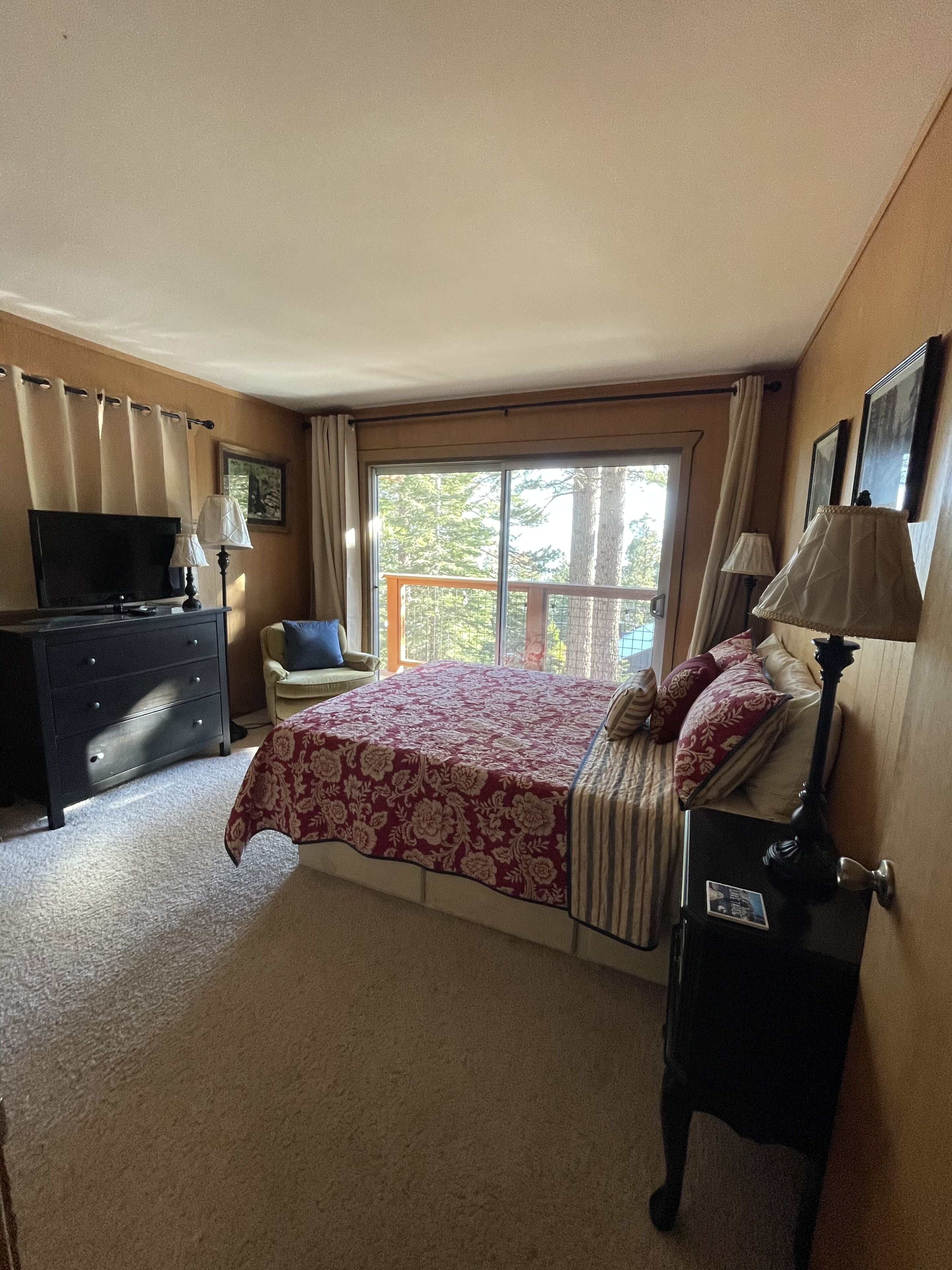 A bedroom with a bed, a dresser, a chair, a television, and a window with curtains.