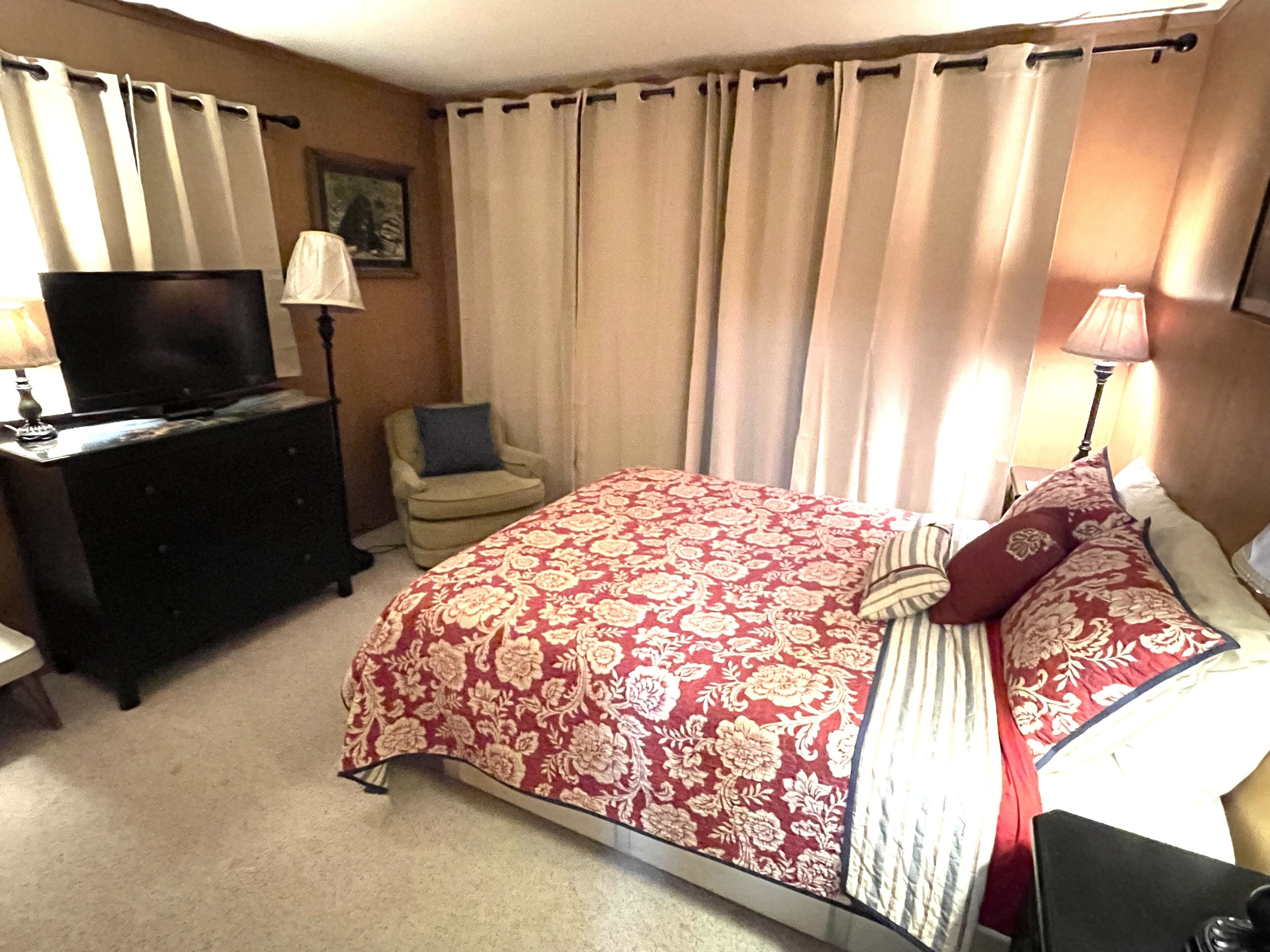 A bedroom with a bed, a TV on a dresser, a chair, and curtains.