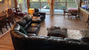 A spacious living room with a leather sectional sofa, wooden dining table, and a large window with curtains. - Tahoe City Cabin~Spectacular Lake View! Walk to Lake and City * WIFI* (Tahoe City)