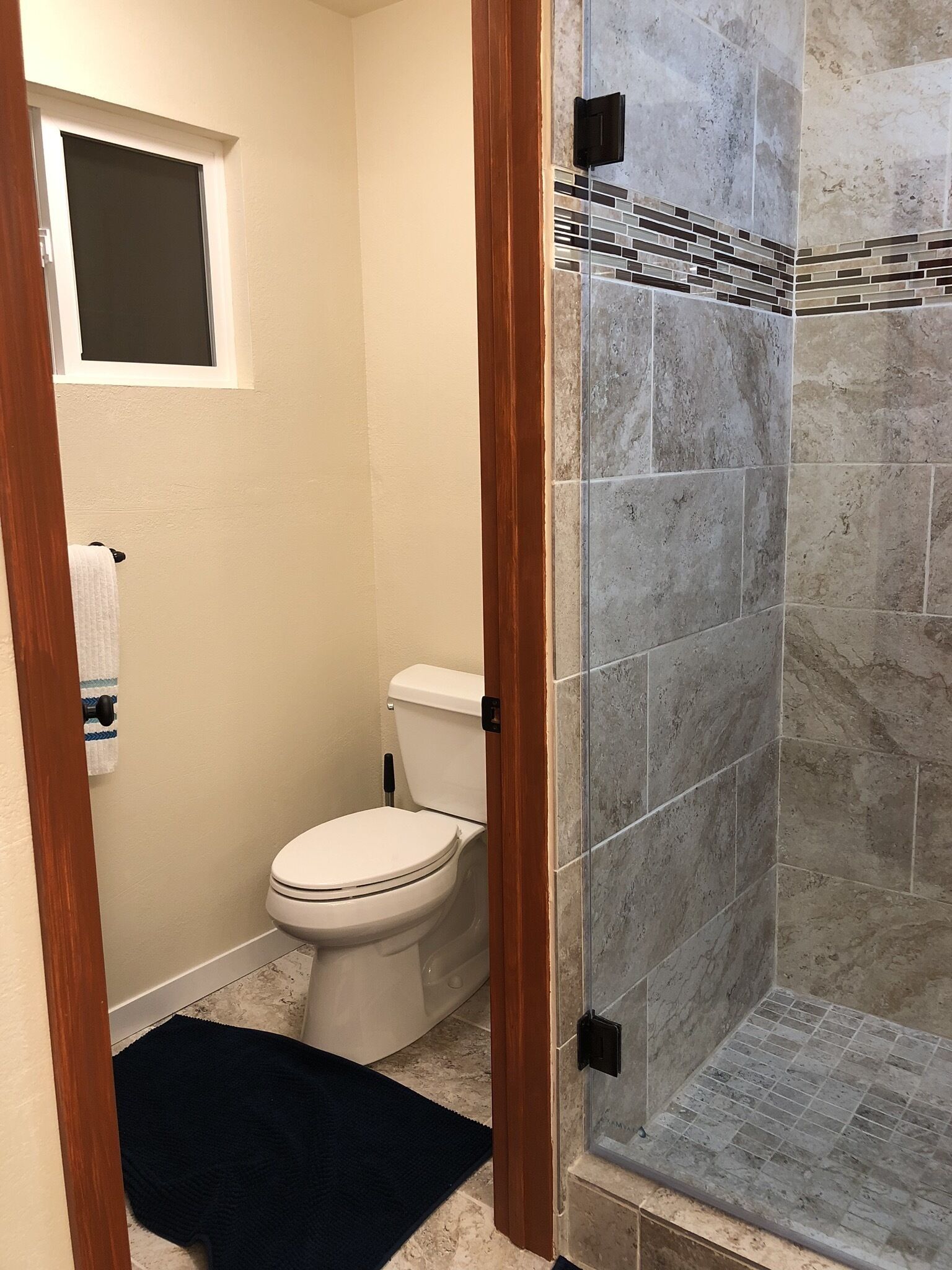 A bathroom with a toilet, a small window, and a shower area with tiled walls.