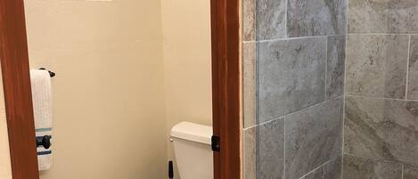 A bathroom with a toilet, a small window, and a shower area with tiled walls.