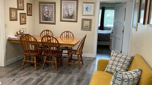 A dining area with a wooden table and chairs, a yellow sofa with patterned cushions, and a small round table with a metal base. - Downtown Bellingham Apartment (Bellingham)
