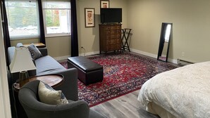 A hotel room with a bed, a sofa, a desk, a TV, and a large window with curtains. - Downtown Bellingham Apartment (Bellingham)