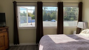 A hotel room with a bed, a TV, a window with curtains, a lamp, and a parking lot view. - Downtown Bellingham Apartment (Bellingham)