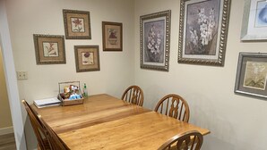 A dining room with a wooden table and chairs, framed floral artwork on the wall, and a basket of snacks on the table. - Downtown Bellingham Apartment (Bellingham)