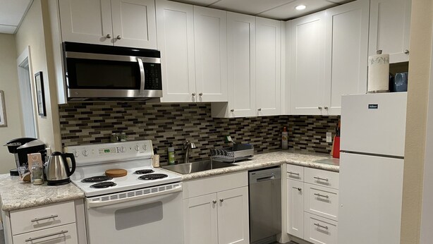 A modern kitchen with white cabinetry, a stainless steel microwave, a stove, and a dishwasher. - Downtown Bellingham Apartment (Bellingham)