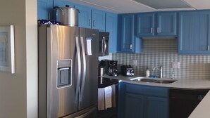 A kitchen with blue cabinets, a stainless steel refrigerator, a microwave, and a coffee maker.