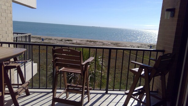 A balcony with a view of the sea, featuring wooden chairs and a table.