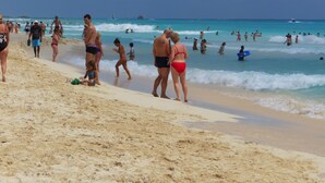 Een druk strand met mensen die langs de kust wandelen en anderen in het water.