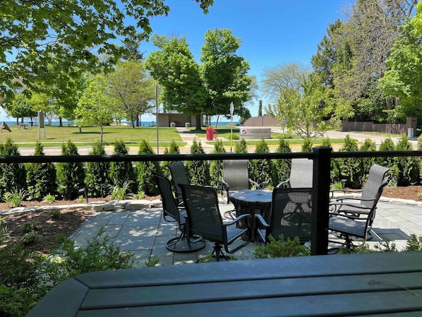 An outdoor patio with chairs and a table, surrounded by greenery and a view of a park.
