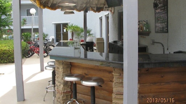 An outdoor bar area with a stone counter and metal stools, a menu board, and a view of the street with parked motorcycles.