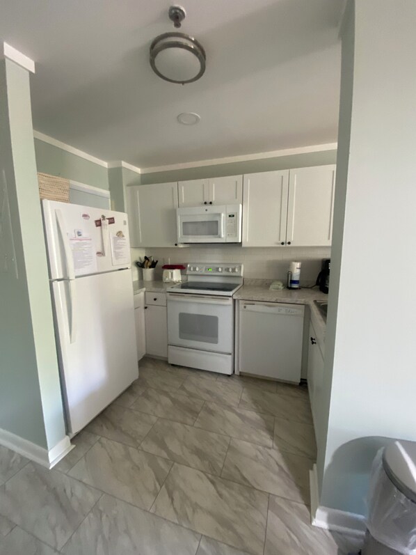 Cocina compacta con electrodomésticos blancos, que incluyen un refrigerador, microondas, estufa y lavavajillas.