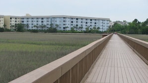 A long wooden bridge leading to a modern apartment building with a flat roof and multiple balconies.