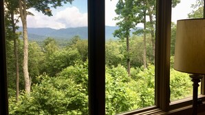 Habitació amb finestra gran que ofereix vistes a un bosc i muntanyes.