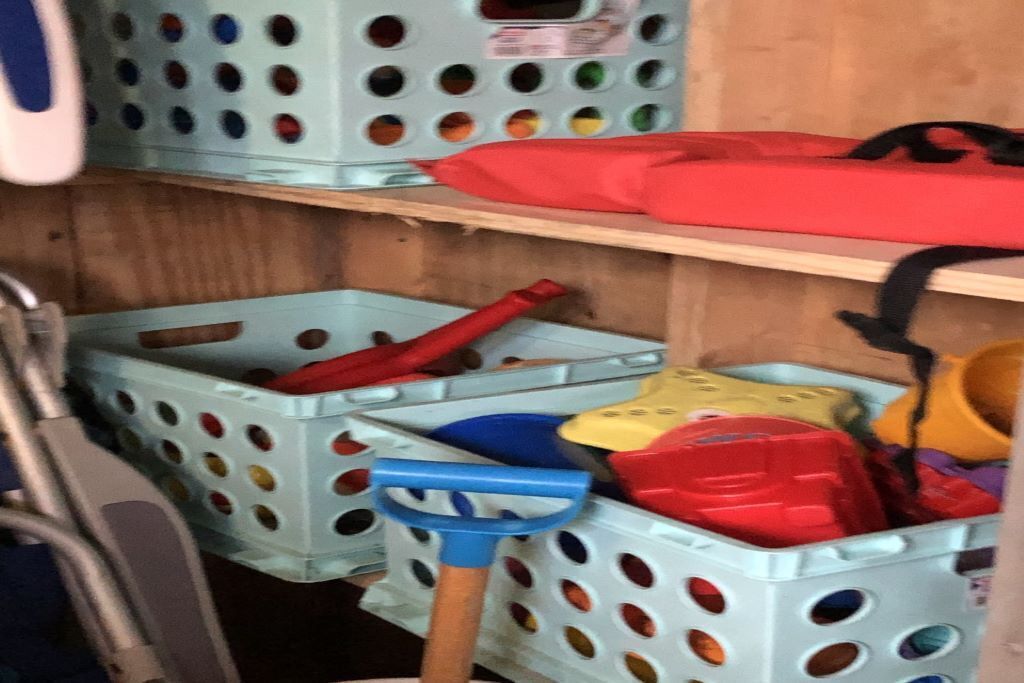 A storage area with plastic baskets containing various items like a blue shovel, red and yellow containers, and a red bag.