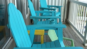 A wooden deck with turquoise Adirondack chairs and a small table.