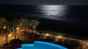 A nighttime view of a pool area with a crescent moon in the sky, overlooking the ocean.