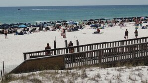 A beach with a wooden boardwalk leading to the water, umbrellas, and people relaxing on the sand.