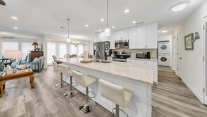 A modern kitchen with bar stools, a dining area with a table and chairs, and a laundry room with stacked washers and dryers.