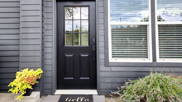 Une maison à l’extérieur d’un gris foncé, avec une porte d’entrée noire et un petit paillasson sur lequel est écrit « bonjour ».