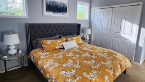 Une chambre à coucher avec un lit, un ventilateur de plafond, une fenêtre, une porte et un tableau encadré au mur.