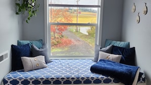 Une pièce dotée d’une banquette intégrée, d’une plante suspendue et offrant une vue sur un paysage rural par le biais d’une fenêtre.