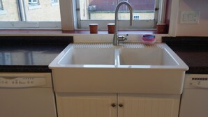 Een keuken met een witte spoelbak, een raam erboven en uitzicht op gebouwen.
