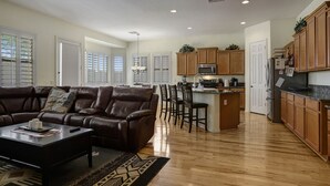 A spacious living room with a leather sofa, a coffee table, and a kitchen area with wooden cabinets and a central island. - 2400 sq. ft., 4 bedroom, 2 bath, sleeps 8, hot tub (Goodyear)