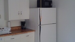 Une cuisine avec des meubles blancs, un réfrigérateur, un four à micro-ondes et un ventilateur de plafond.