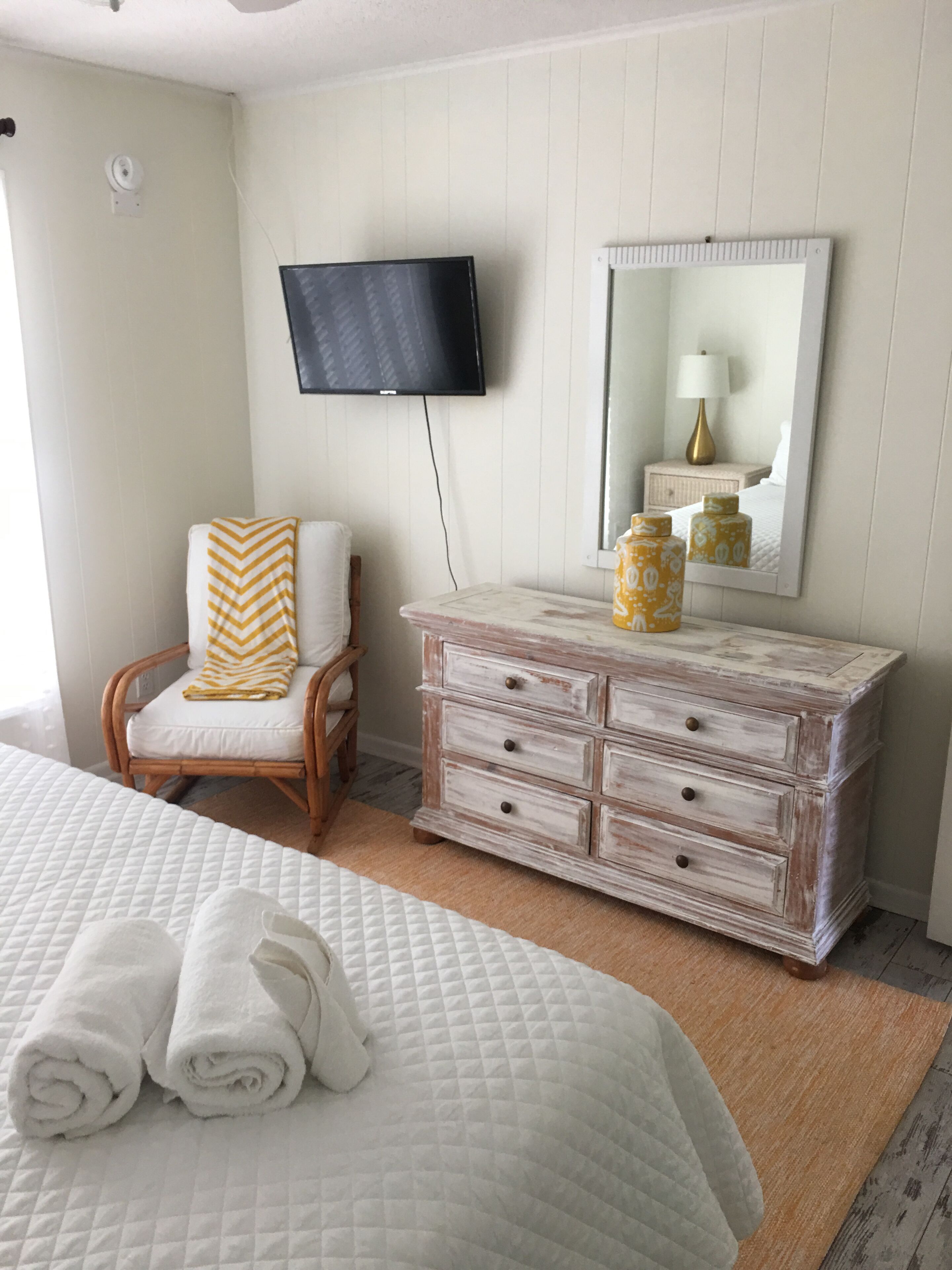 A bedroom with a bed, a chair, a dresser, a television, and a mirror.