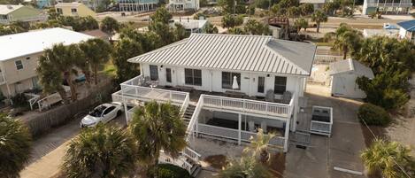 A two-story house with a balcony, a car parked in front, and surrounding palm trees.
