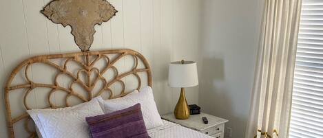 A neatly made bed with a white quilt, a purple pillow, and two rolled towels.