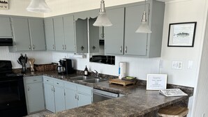 A kitchen with granite countertops, two bar stools, a black stove, and a stainless steel sink. - East End -Beach Oasis- St. George Island. Beach Condo / Full Sized Swimming Pool (St.George Island)
