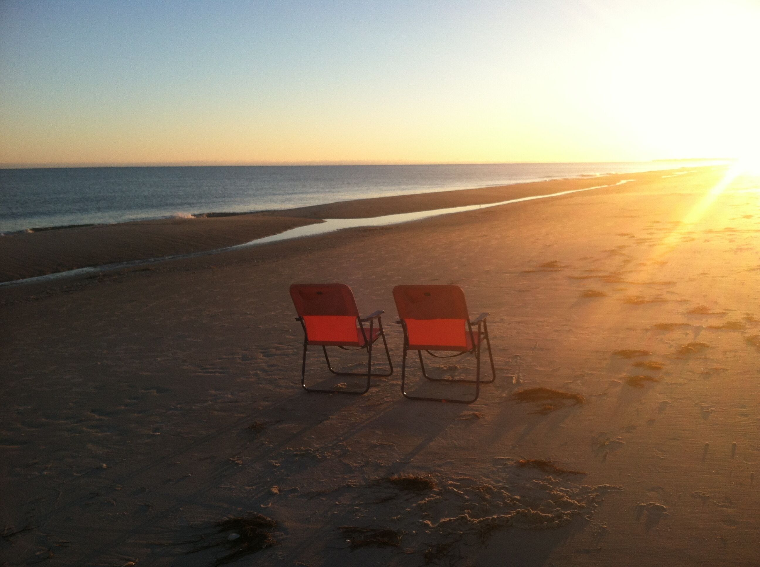 Due sedie da spiaggia rosse che si affacciano sull'oceano al tramonto.