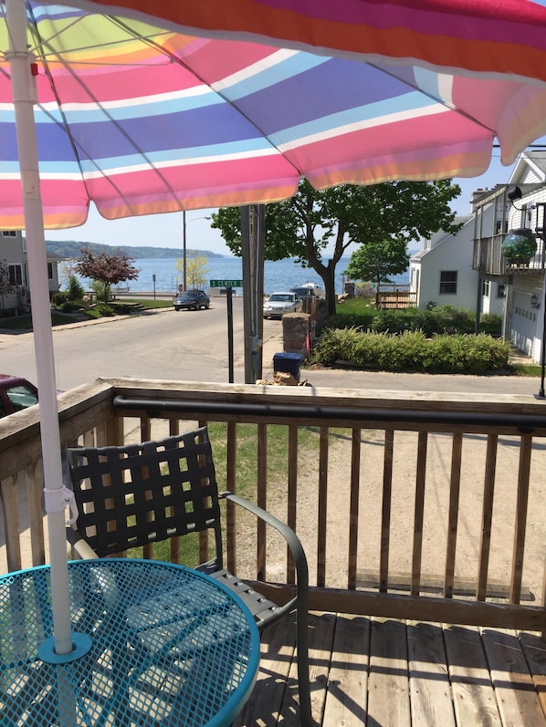 A wooden deck with a metal chair and a table, an umbrella, and a view of a street and lake.