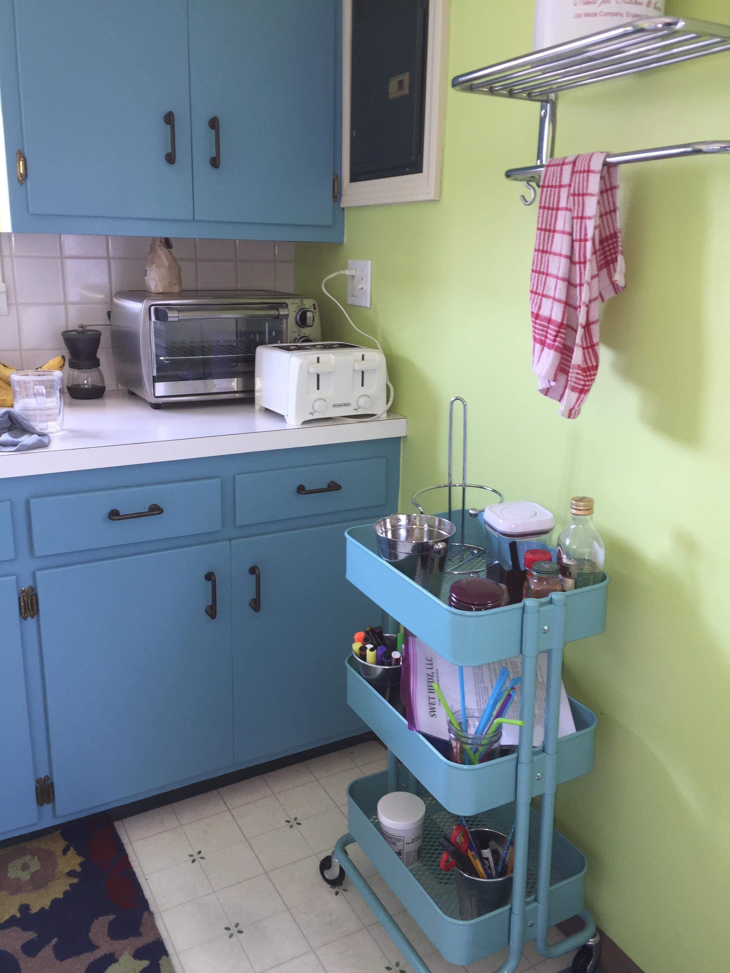 A kitchen with blue cabinets, a toaster, a kettle, and a metal rack with a cloth.