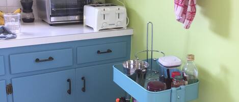 A kitchen with blue cabinets, a toaster, a kettle, and a metal rack with a cloth.