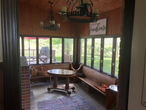 A cozy room with a large window, a wooden bench, a table, and a chandelier.