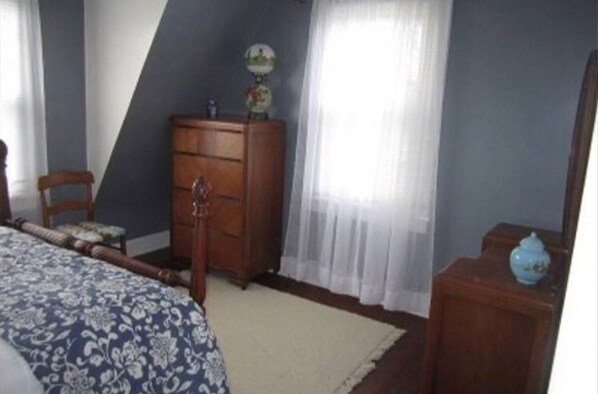 A bedroom with a bed, a wooden dresser, a chair, and a small table with a globe.