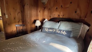 A wooden room with a bed, a nightstand, and a chair. - Peaceful Lakefront Retreat with Views (Newfield)