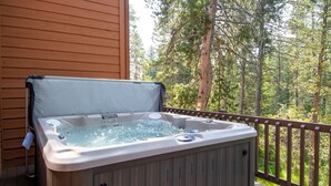 Un jacuzzi en una terraza de madera con barandilla, rodeado de árboles.