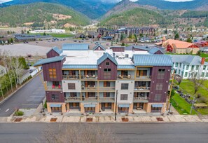 A multi-story hotel with balconies, a parking lot, and a mountainous backdrop. - Large Condo Full Kitchen - 2 Beds, Mtn Views, Hot tub, Sauna, on Bike Trail (Kellogg)