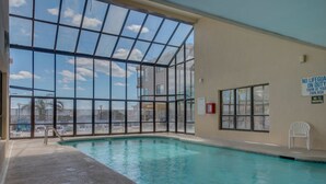 An indoor swimming pool with clear glass walls, lounge chairs, and a view of a building outside. - Oceanfront Condo with indoor pool + Free Attraction Tickets! (North Myrtle Beach)